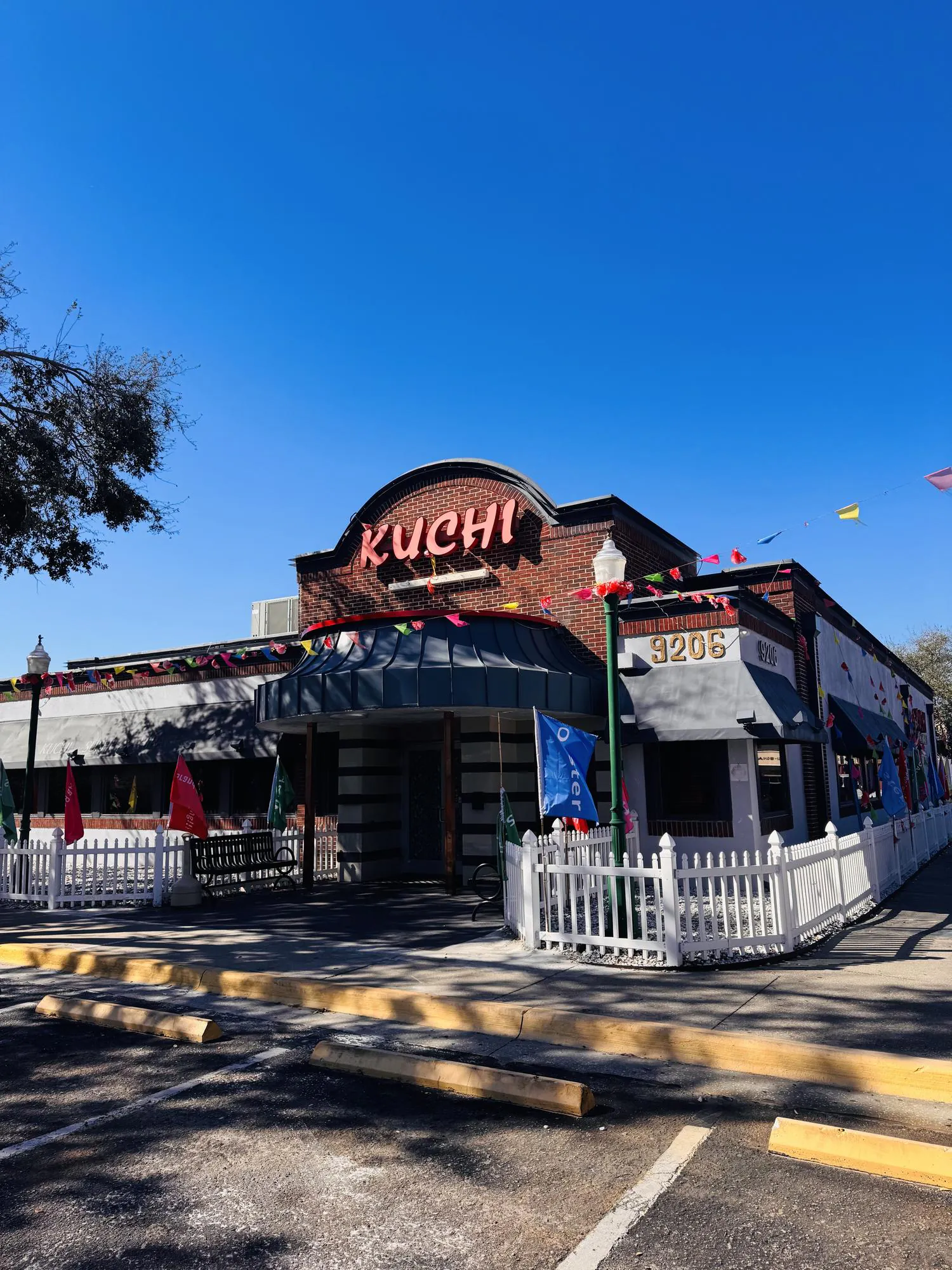 Charming brick exterior with festive flags and white picket fence at Kuchi, a Buffet Restaurant in Tampa